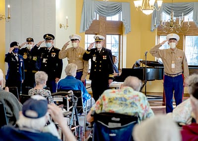 Military personnel salute in front of an audience of seniors