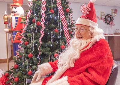 Senior man in Santa suit poses next to Christmas tree