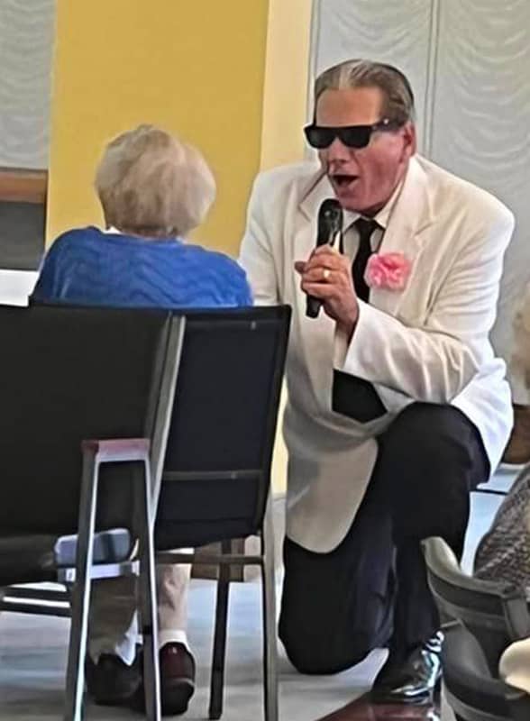 Entertainer on his knees sings to elderly woman in chair
