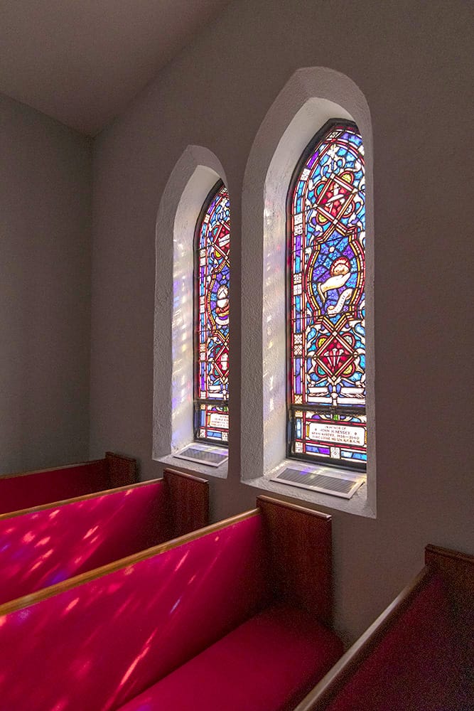 Sunlight shining through stained glass window casting a multicolor pattern on pews