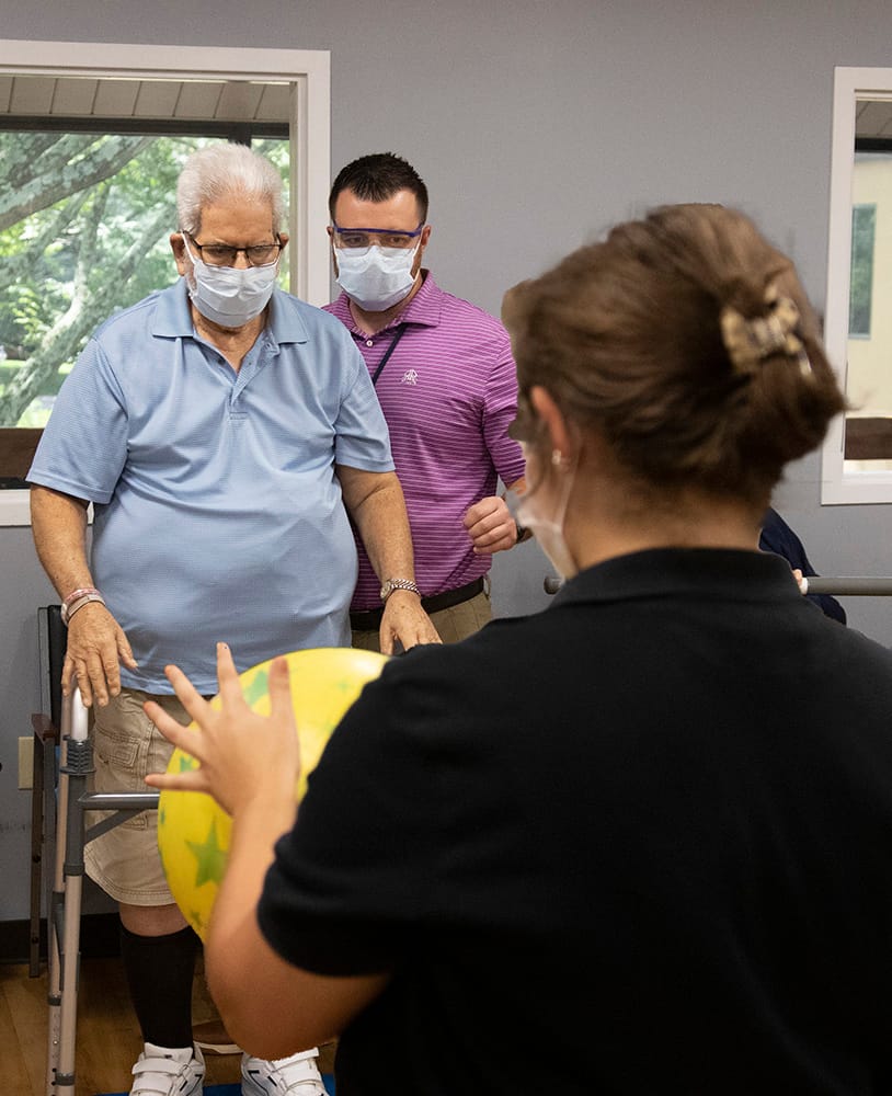 Physical therapist helps older man with an exercise using a ball