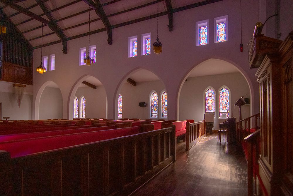 Interior of a large chapel with sunlight shining through stained glass windows